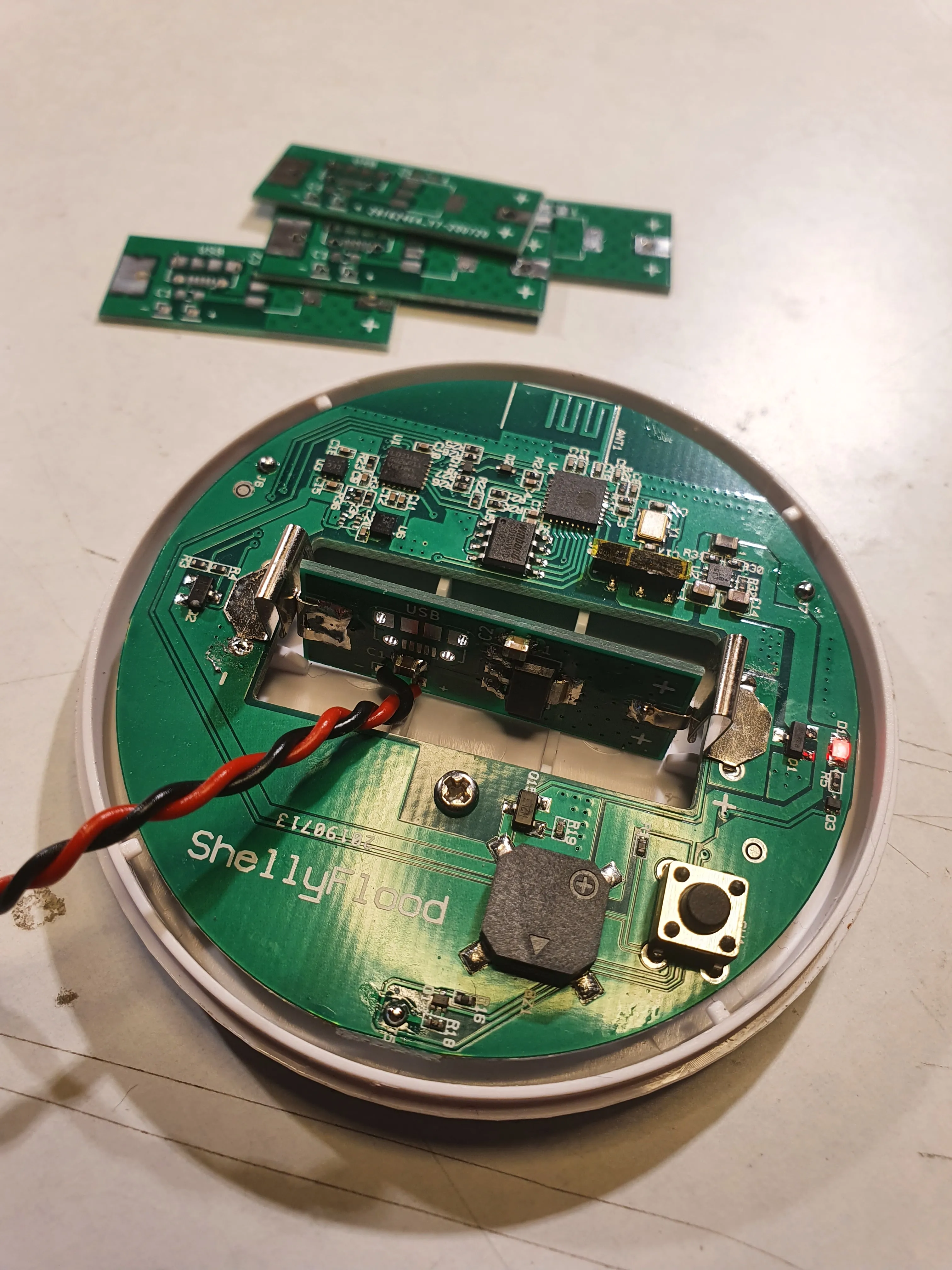 A Shelly Flood sensor opened up with the adapter board fitted in its CR123 battery bay and a power lead run out, with three spare boards above